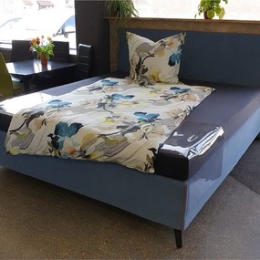 Modernes Boxspringbett mit blauer Polsterung und floral gemusterter Bettwäsche im Showroom.